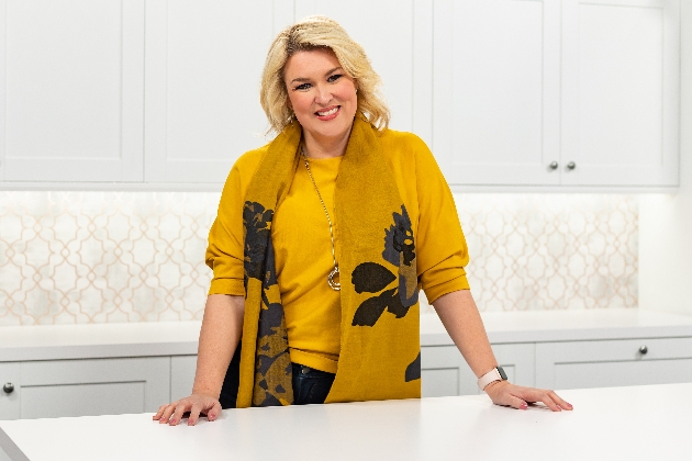 Sara Davies at her crafting station wearing a yellow sweater