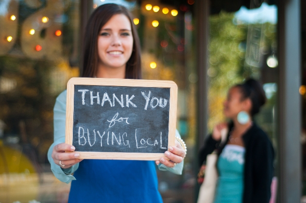 woman outside shop holding a sign 'thank you for shopping local'
