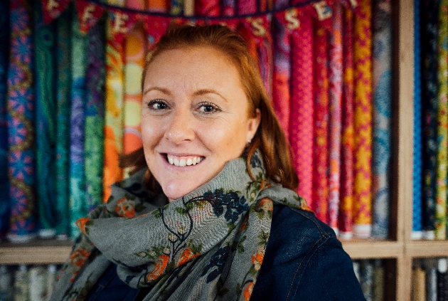 lade in denim jacket and scarf standing in the shop surrounded by fabrics