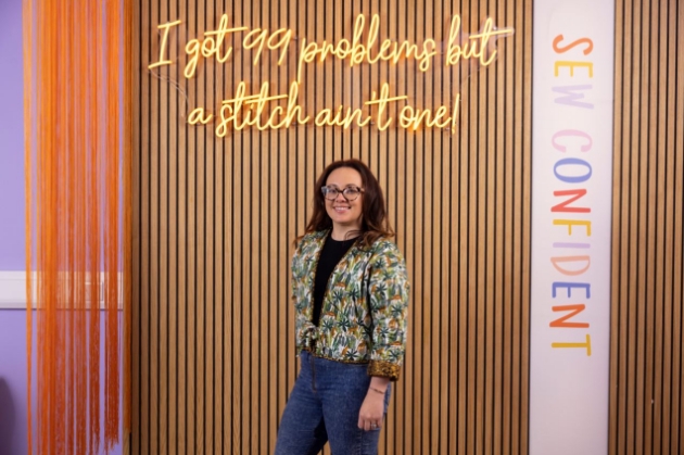 brunette lady standing under neon sign next to Sew Confident banner