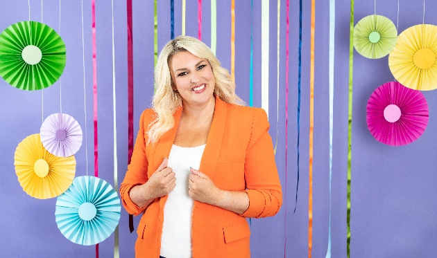 Sara Davies in orange dress in front of paper streamers