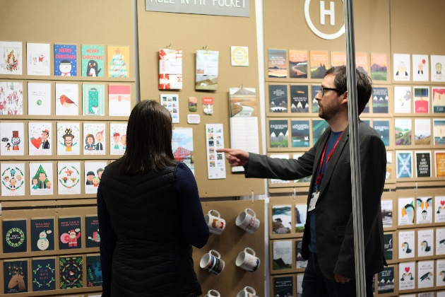 Man showing lady greeting card on a wall in an exhibition centre