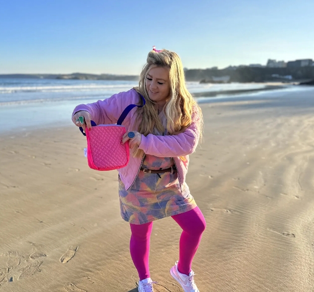 Blonde female holding sustainable pink bag on a beach