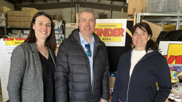 three people standing front of table full of donated stationery supplies