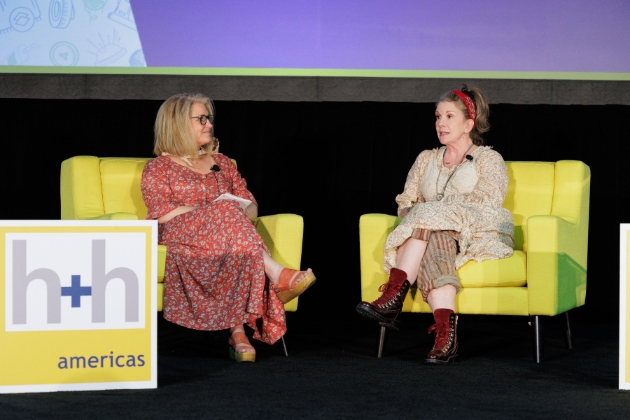 two women on yellow chairs on a stage having a discussion