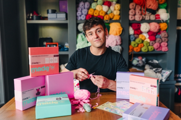 Tom Daley sitting at craft table with his crochet box sets