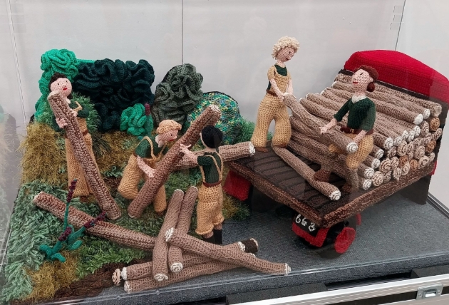 knitted artwork of people carrying logs